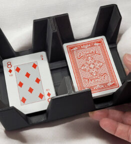 Hand picking up 2 of spades from a 6 deck card tray on wood table